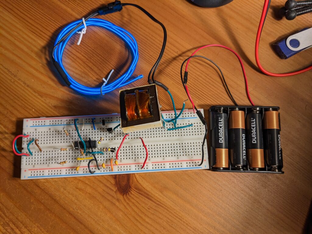 A circuit on a breadboard, powered by 4 AA batteries, driving a 1m coil of blue EL-wire.