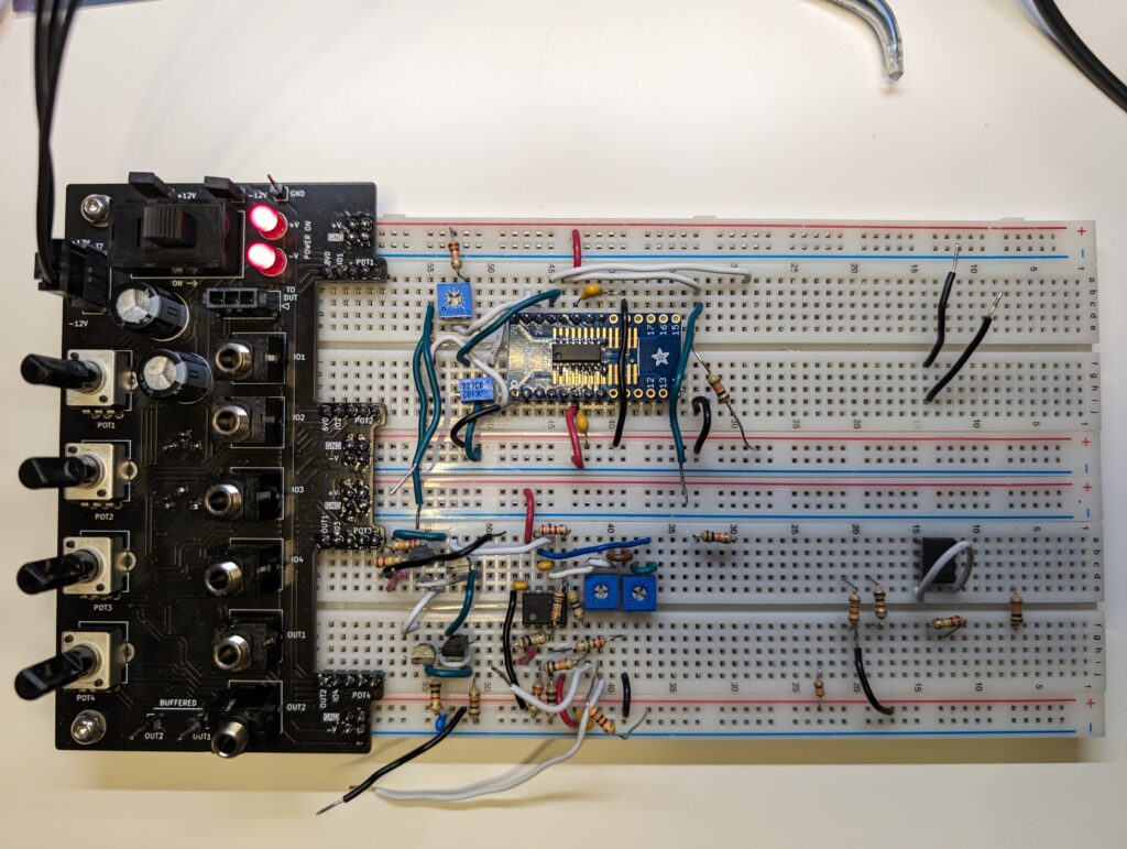 A PCBA with a switch, two LEDs, four potentiometers, and six 3.5mm jacks is affixed to the left side of two breadboards, via headers pins inserted into various rows on the breadboards. 

There is another circuit being prototyped on the breadboard itself with resistors, transistors, capacitors, and some ICs.