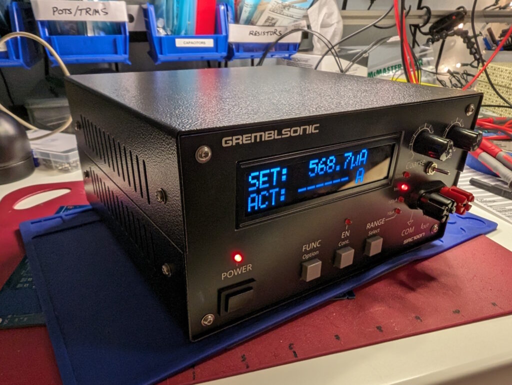 The assembled project in its case sits on a workbench. A brightly lit screen reads "SET: 568.7uA".
Two potentiometers some buttons, LEDs, and a pair of banana jacks are on the front panel along with their labels.