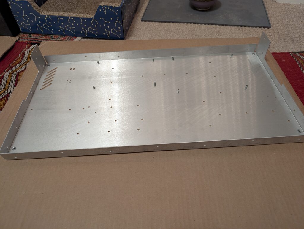 The bottom panel, with sides folded up to make an open box shape. There are many holes drilled in the bottom for mounting elements, and some press fit standoffs and nuts are installed.